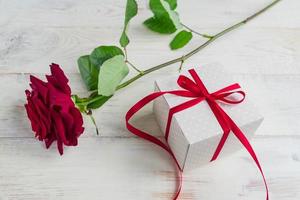 Beige polka dot gift box with red ribbon bow and bautiful red roses on wooden background. Greeting card for holiday. photo