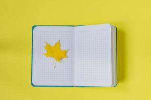 cuaderno abierto en blanco con hoja de arce sobre fondo amarillo. diario vacío y concepto de otoño foto