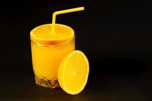 jugo de naranja fresco y saludable en un vaso con cítricos alrededor sobre fondo negro foto