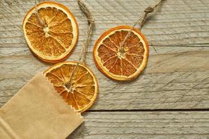 Christmas decor. Dried orange slice in craft paper package on wooden background, top view, minimal flat lay photo