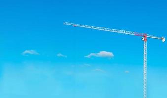 Construction cranes work on creation site against blue sky background. Bottom view of industrial crane. Concept of construction of apartment buildings and renovation of housing. Copy space photo