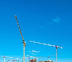 Construction cranes work on creation site against blue sky background. Bottom view of industrial crane. Concept of construction of apartment buildings and renovation of housing. Copy space photo