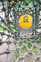 Inside view of a long rope mesh pipe, at the end of the tunnel yellow playground blurred background photo