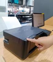 A person is pressing an empty printer on a table with a computer next to it. photo