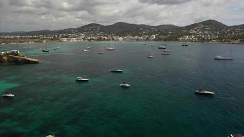 survolez des yachts et des bateaux en eau libre de la côte d'ibiza, des collines verdoyantes en arrière-plan video