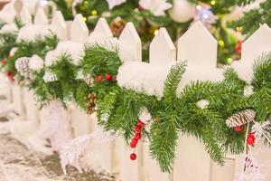 Close up of white fence decorated with christmas garland with cones and snow. Backyard festive decoration. photo