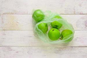 Fresh green apples in plastic bag on wooden table. environmental concept of non-ecological use of plastic photo