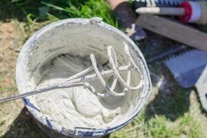 mixing tile adhesive or cement with a power drill for repair works on construction site photo