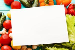 concepto de comida. menú del restaurante. papel de receta en blanco y plantilla con verduras en la mesa azul. vista superior y macro. copie el espacio Bosquejo foto