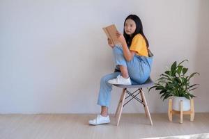 la niña sentada en una silla sosteniendo un libro en una habitación mínima. foto