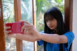 Happy young girl using mobile phone and sitting on the windows at home. photo