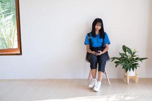 niña sentada en la silla y usando el teléfono móvil en la habitación. foto