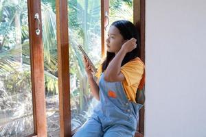 la niña sostiene el libro sentado en las ventanas de madera en casa. foto