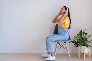 la niña feliz sentada en una silla escuchando música en una habitación mínima en casa. foto