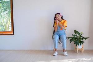 la niña feliz sentada en una silla escuchando música en una habitación mínima en casa. foto