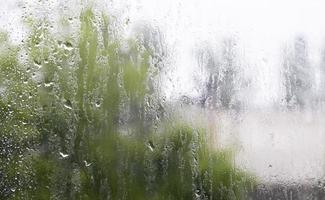 Heavy rain. Raindrops on the window glass on a summer day. Selective focus, shallow depth of field. Drops of water fall on a wet window. Glass full of drops during a downpour. photo