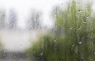 Heavy rain. Raindrops on the window glass on a summer day. Selective focus, shallow depth of field. Drops of water fall on a wet window. Glass full of drops during a downpour. photo