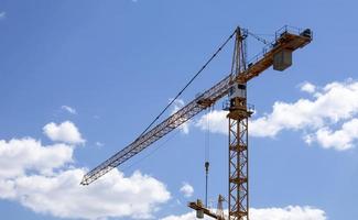 A working construction tower crane against a cloudy sky on a sunny day. The concept of urban development and construction. Industrial background. Crane engineering, construction industry tool. photo