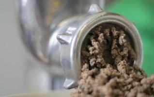 Minced meat in a manual mechanical meat grinder. Fresh boiled meat is ground with an old metal meat grinder, close-up in the kitchen. photo