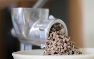 Minced meat in a manual mechanical meat grinder. Fresh boiled meat is ground with an old metal meat grinder, close-up in the kitchen. photo