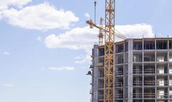 A working construction tower crane against a cloudy sky on a sunny day. The concept of urban development and construction. Industrial background. Crane engineering, construction industry tool. photo