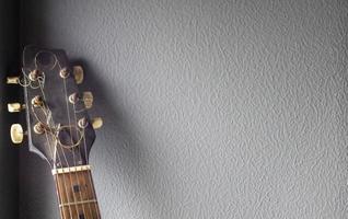 An acoustic old guitar in dust stands against a gray wall with copy space. Background for a screensaver with a musical instrument in the old style. photo