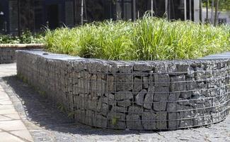 Muro de soporte de canasta hecho de gaviones de granito. gaviones en el jardín. cerca de gaviones moderna con piedras en malla de alambre. Cercado de malla de alambre de gaviones con piedra natural y arbustos. foto