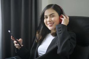 joven mujer de negocios relajante usando teléfono inteligente y escuchando música en la oficina moderna. foto