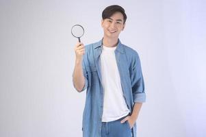 Young asian man holding magnifying glass over white background, analysis and finance concept. photo