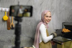 Beautiful muslim woman is making bakery while live streaming or recording video on social media in her house, coffee shop business concept. photo