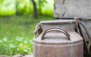 One old rusty metal can in the countryside. Container for transporting liquids, milk or liquid fuels with multiple handles. Milk bank of a cylindrical form with a wide mouth. Bottle with sealed cap. photo