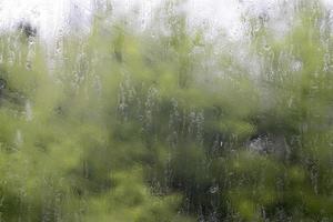 Heavy rain. Raindrops on the window glass on a summer day. Selective focus, shallow depth of field. Drops of water fall on a wet window. Glass full of drops during a downpour. photo