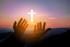 Silhouette of human hands palm up praying and worship of cross, eucharist therapy bless god helping, belief, forgiveness, freedom, hope and faith, christian religion concept on sunset background. photo