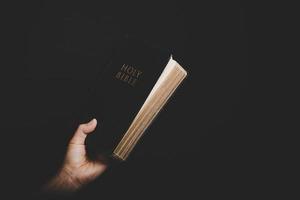 Close up of christian woman hand holding holy bible pray and worship for thank god in church with black background, adult female person are reading book, photo