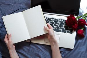 Hands, computer keyboard, bed top view. Workplace background, work at home, notepad and flowers photo