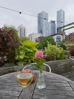 Glass of white wine next to a flower on a table of an outdoor pub with skyscrapers in the distance in Castlefield in Manchester, UK photo