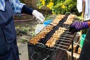 The hands of a merchant grilling pork skewers are lined up on charcoal grills. photo