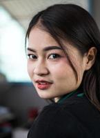 A close-up of a portrait of a beautiful Thai woman smiling seductively inside her coffee shop. photo