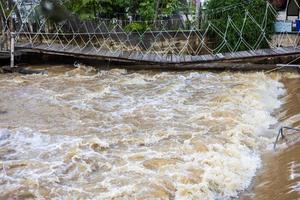 A low view of the river flowing violently past a broken wooden bridge. photo