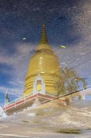 A beautiful golden circular pagoda reflects water on concrete against a backdrop of blue sky. photo