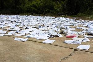 trozos de papel viejo cuadrado de varios cuadernos están esparcidos en el piso de concreto cerca de los arbustos para que se sequen. foto