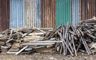Low view, piles of logs of different sizes are piled on the ground near old galvanized walls. photo