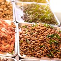 Plenty of fried worms near shrimp and others are piled up in stainless steel trays. photo