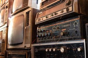 Old and dirty stereo amplifiers and black-and-white televisions are stacked. photo