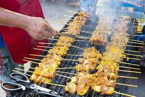 The hands of a merchant grilling pork skewers are lined up on charcoal grills. photo