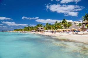 People swimming near white sand beach with umbrellas, bungalow bar and cocos palms, turquoise caribbean sea, Isla Mujeres island, Caribbean Sea, Cancun, Yucatan, Mexico photo