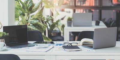 Laptop Computer, notebook, and eyeglasses sitting on a desk in a large open plan office space after working hours photo