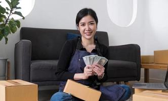 mujer joven independiente que trabaja y tiene dinero con una caja de cartón en casa - pyme negocio en línea y concepto de entrega foto