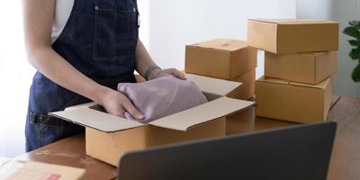 Startup small business entrepreneur SME, asian woman packing shirt in box. Portrait young Asian small business owner home office, online sell marketing delivery, SME e-commerce telemarket job concept photo