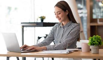 Charming asian businesswoman sitting working on laptop in office. photo